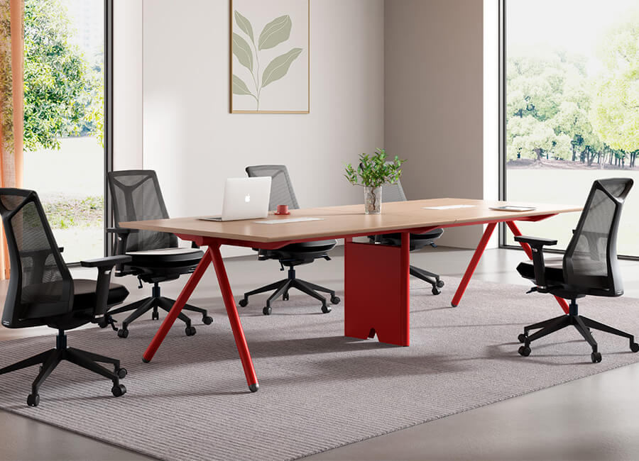 A small conference table with a red corner and 4 black office mesh chairs with wheels